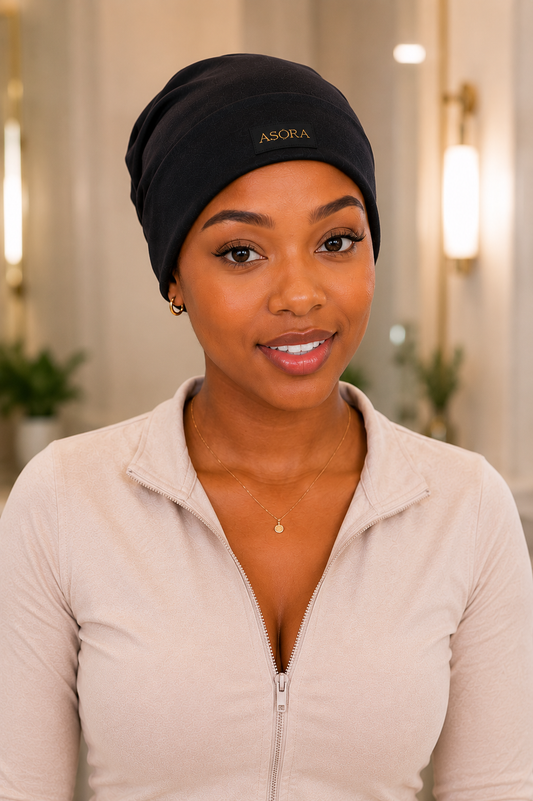 Woman wearing a black cap with 'ASORA' branding, standing indoors.