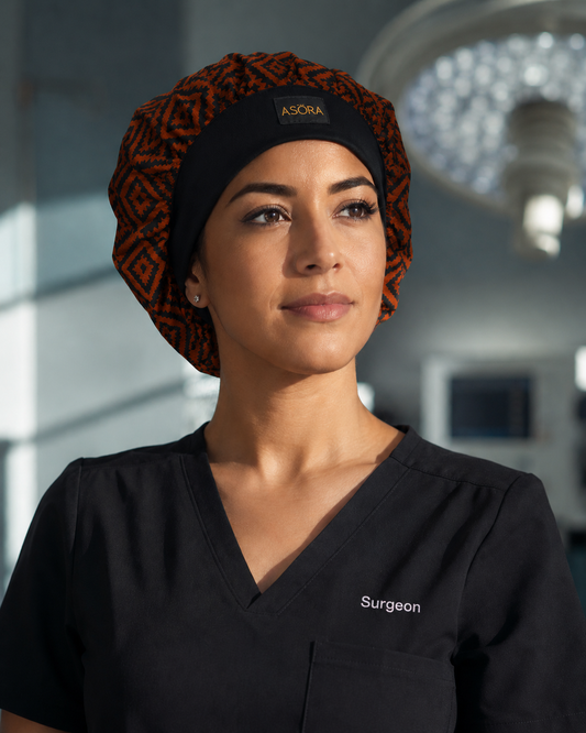 Surgeon wearing a black scrub and ASORA scrub cap top with 'Surgeon' printed on it, standing in an operating room.