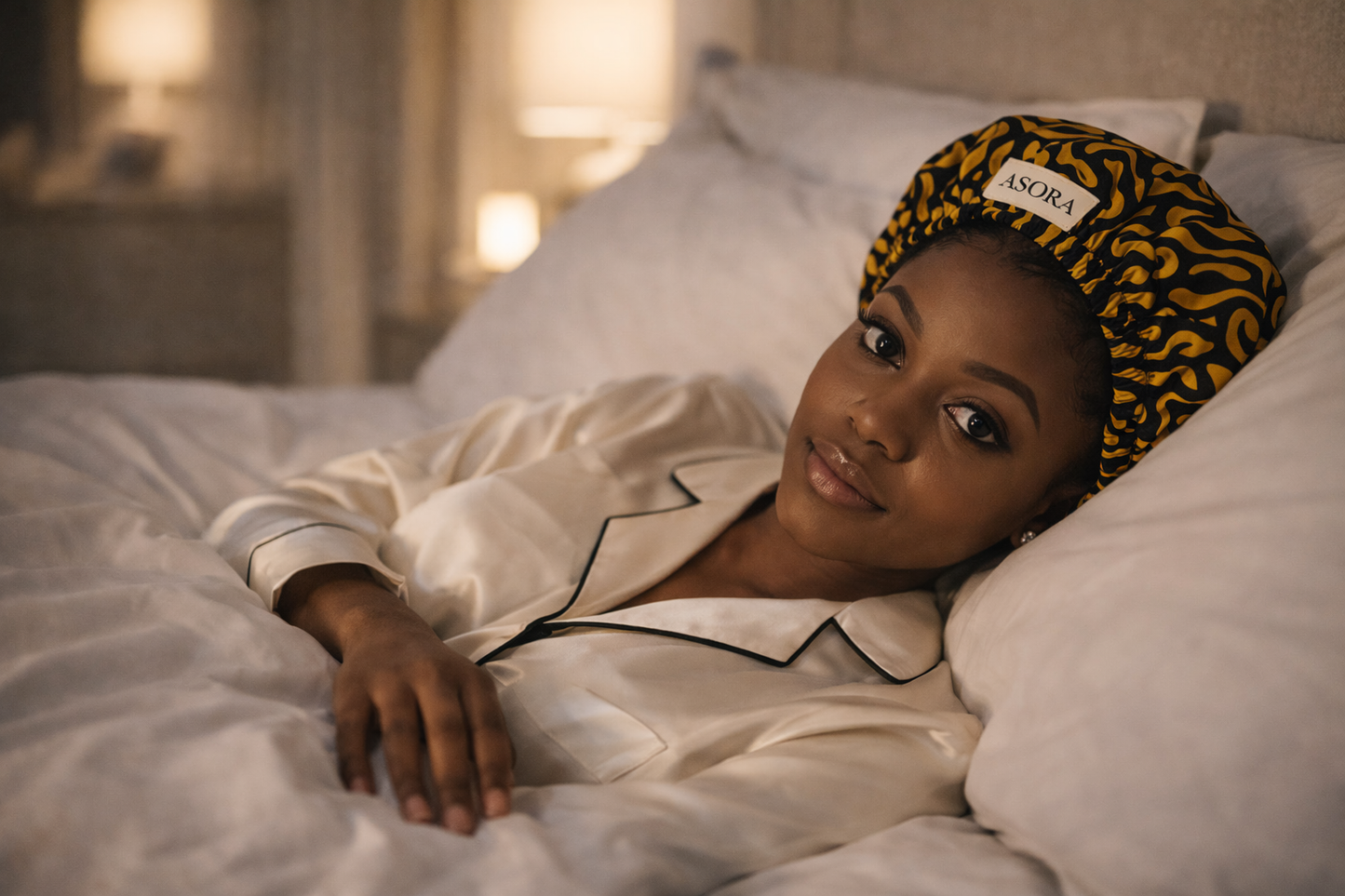 ASORA Ade Bonnet cap,, Woman wearing a patterned headband and pajama set on a bed, with 'ASORA' branding visible.