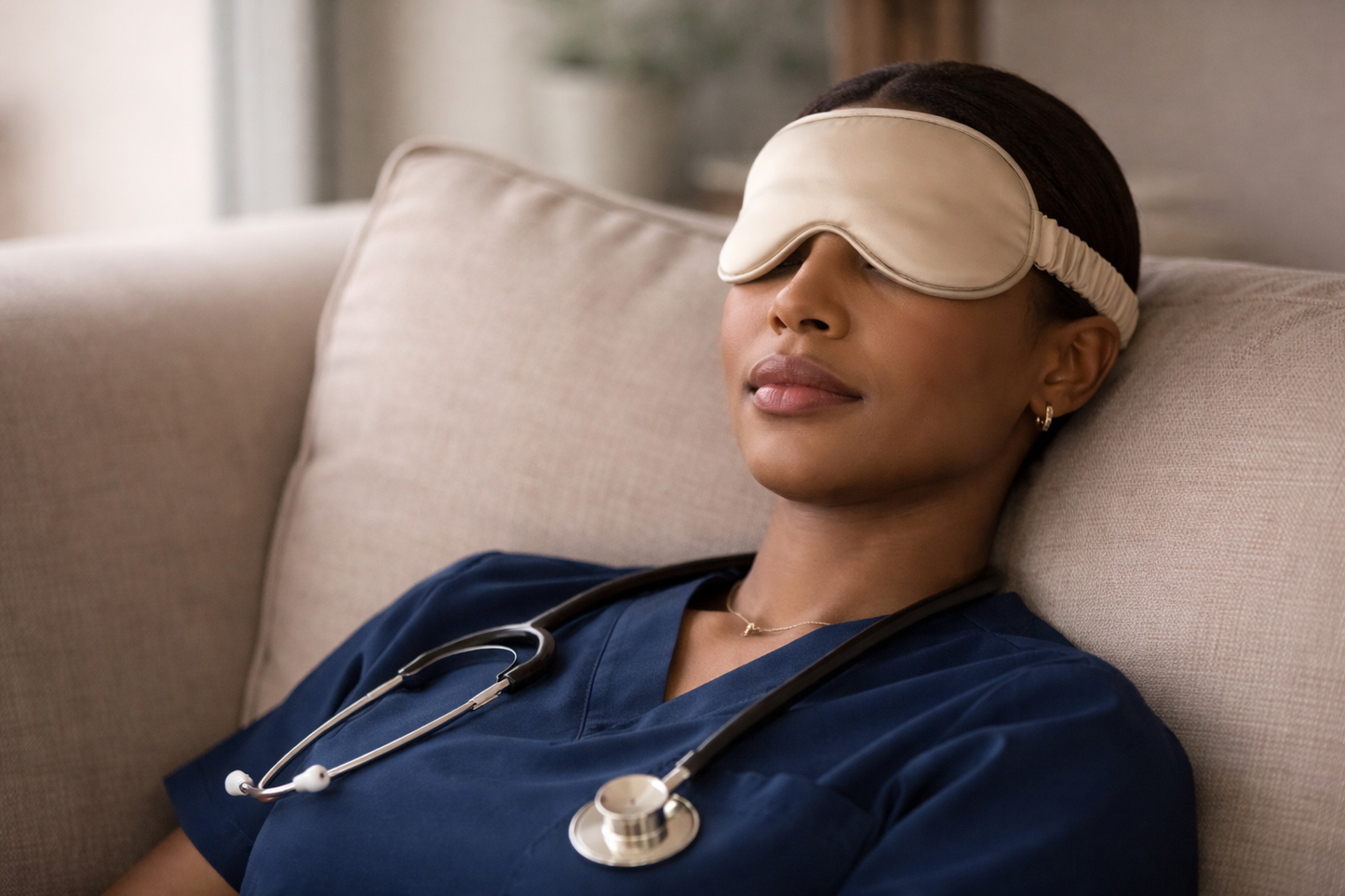 ASORA, Person in blue scrubs with a stethoscope wearing a cream sleep mask, sitting on a beige couch.