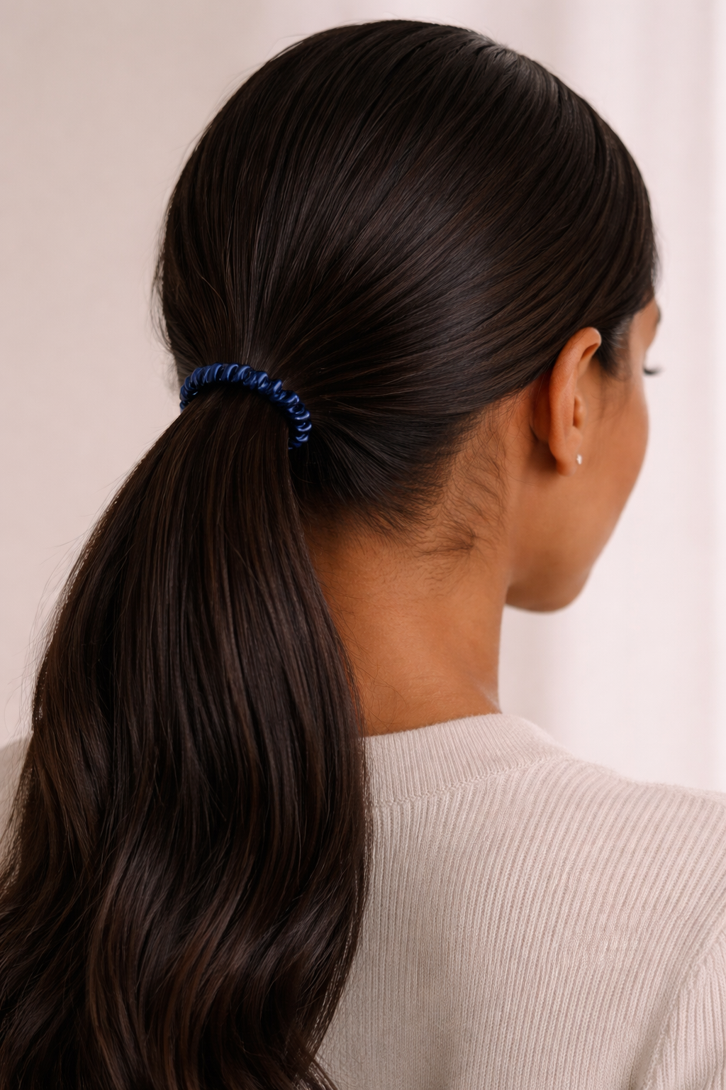 Person with long dark hair mulberry silk skinny scrunchie from ASORA with a blue scrunchie against a neutral background