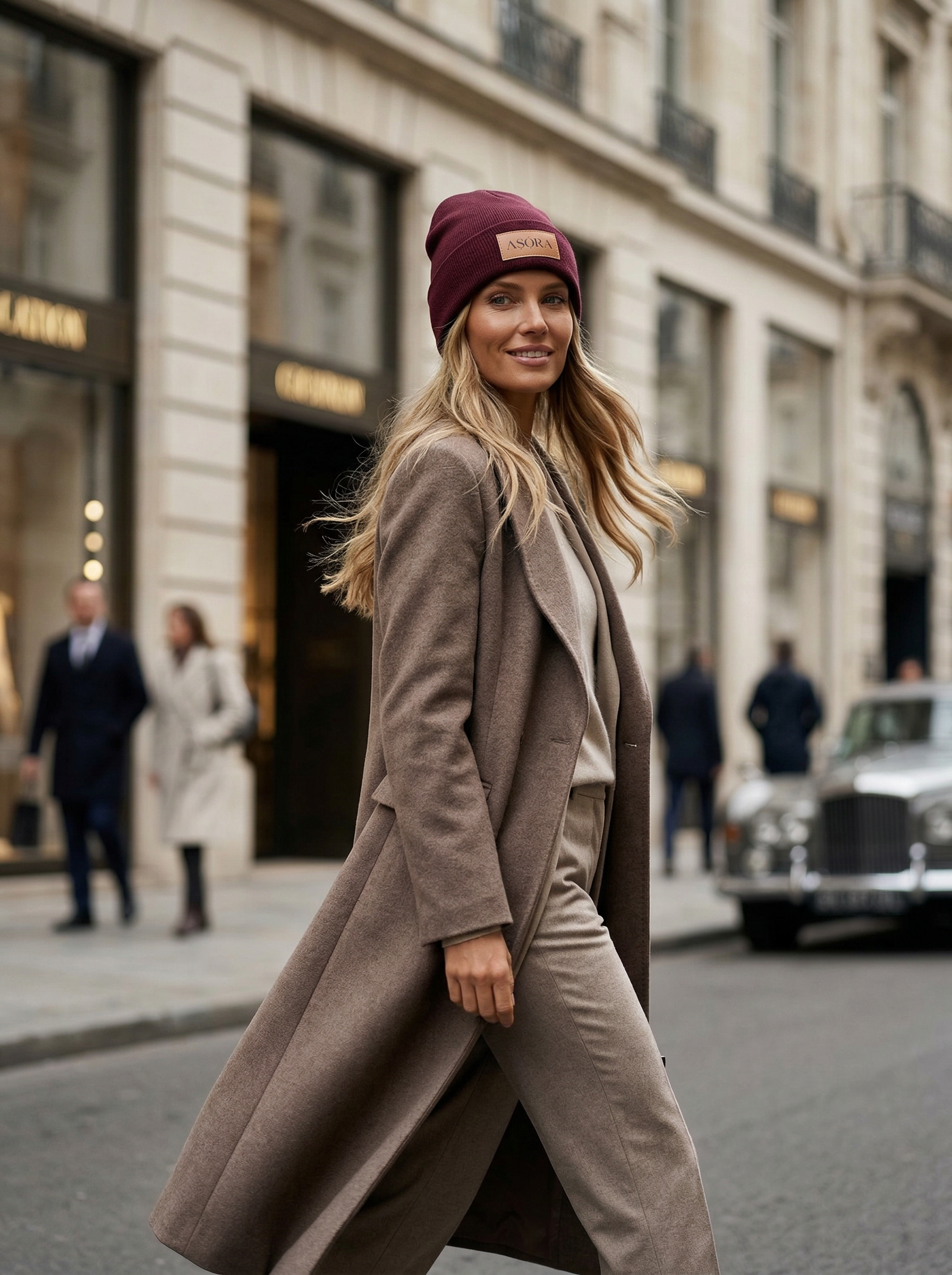 ASORA, Woman in a long coat and beanie walking on a city street.